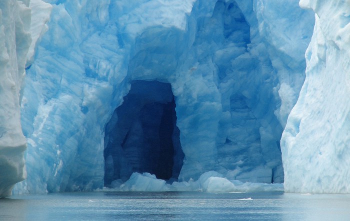An ice cave in a glacier in which the ice is giving off a blue hue.